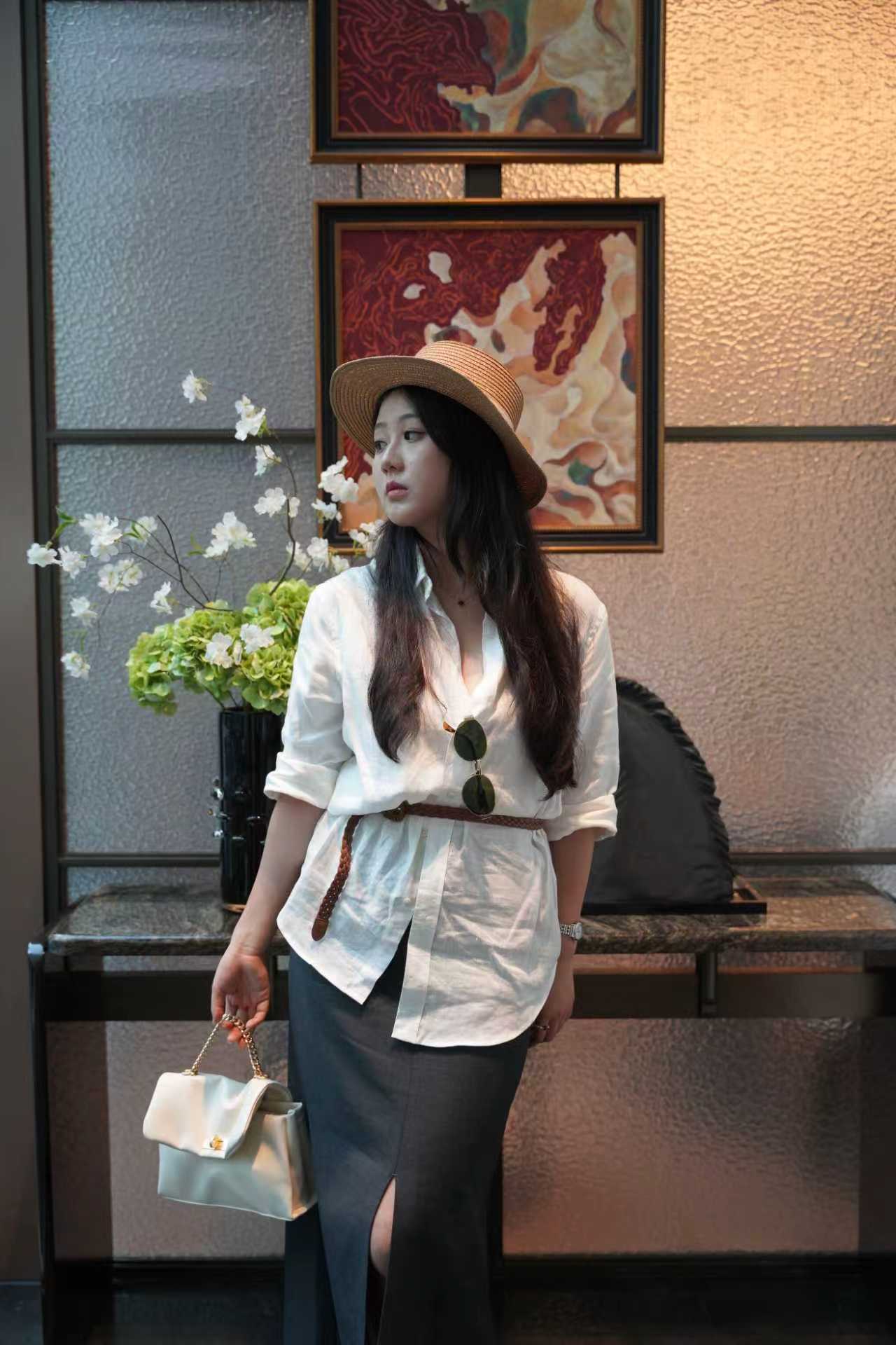 Woman in a white blouse and hat standing in a room with floral arrangements and framed pictures.
